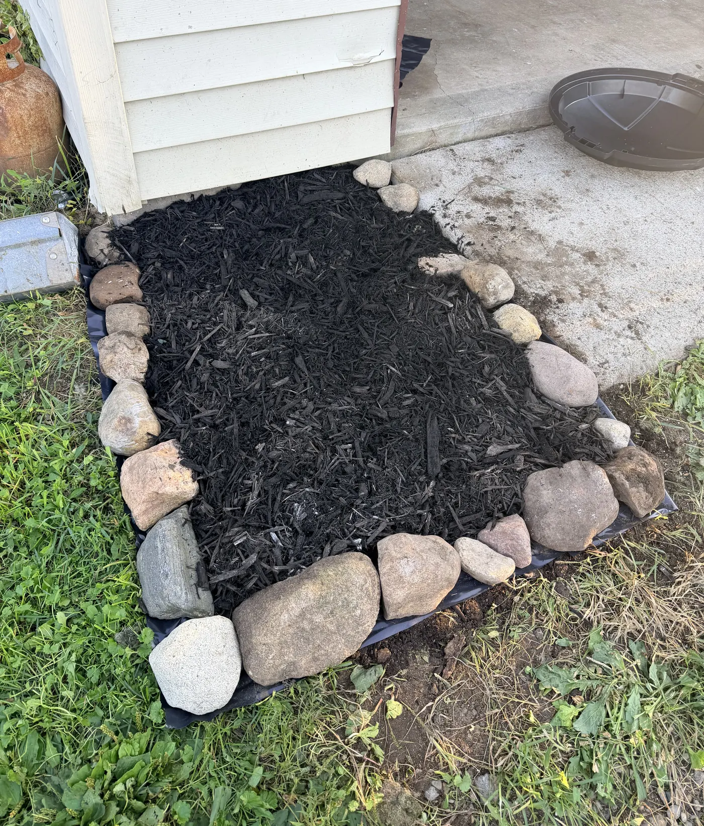 Fresh black mulch bed edged with field stones against a house