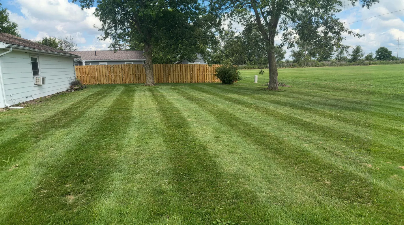 Long side lawn mowed in wide light and dark stripes beside a wooden fence